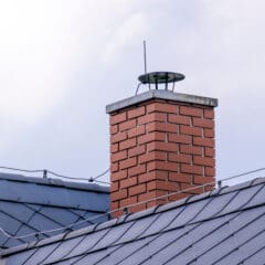 A red brick chimney with a metal cap extends from a gray, sloped metal roof. The sky is cloudy in the background.