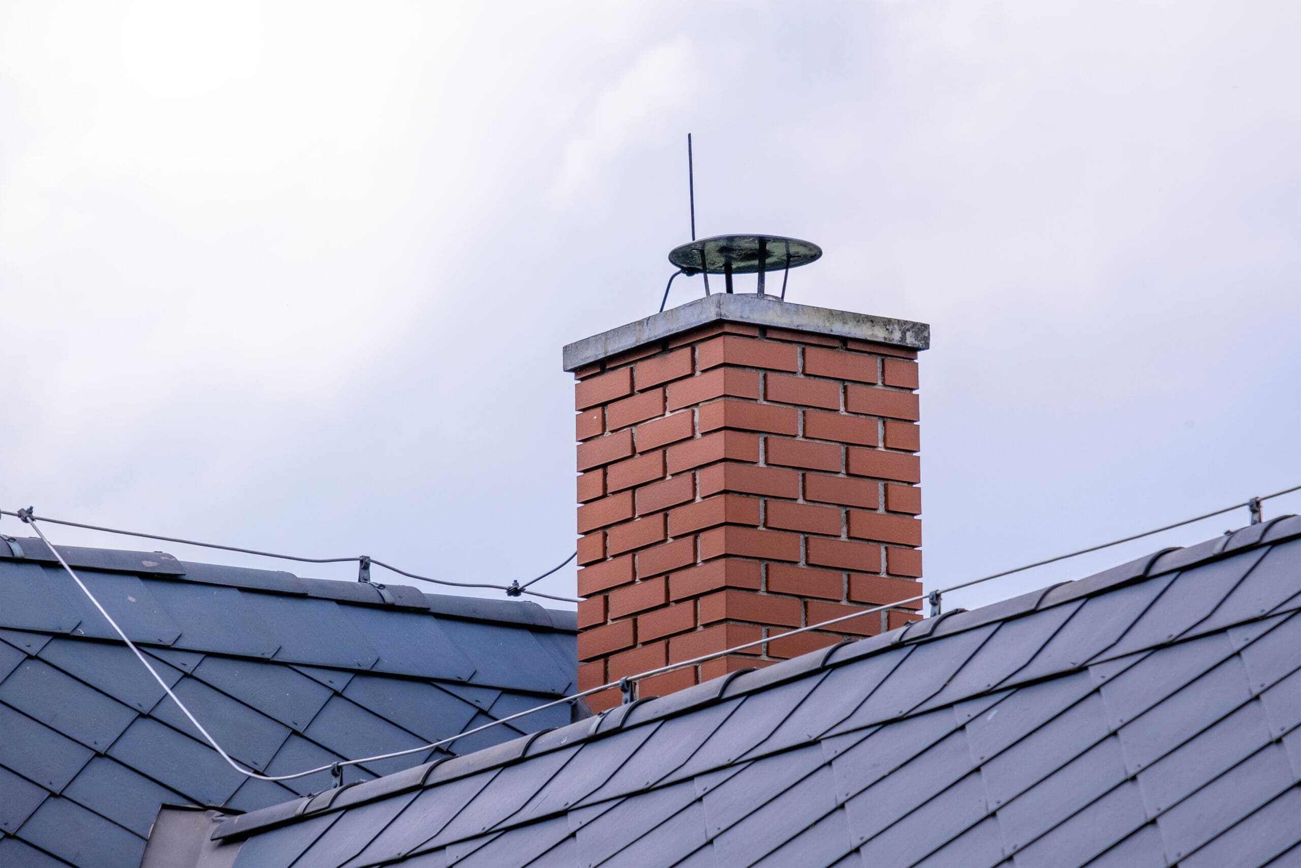 A red brick chimney with a metal cap extends from a gray, sloped metal roof. The sky is cloudy in the background.