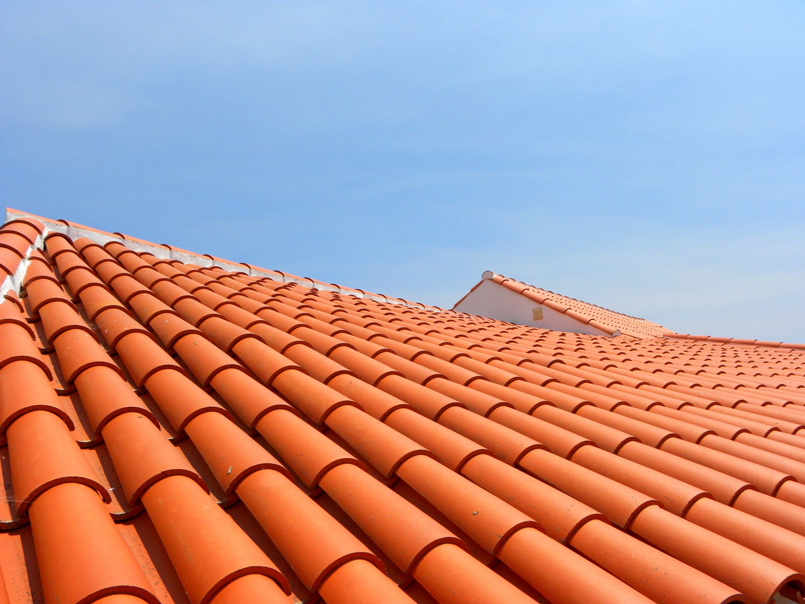 A rooftop covered in orange terracotta tiles under a clear blue sky. The tiles are neatly aligned, creating a pattern, with the roof extending into the distance.